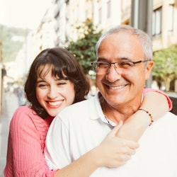 A woman smiles while wrapping her arms around her dad on a sunny day.
