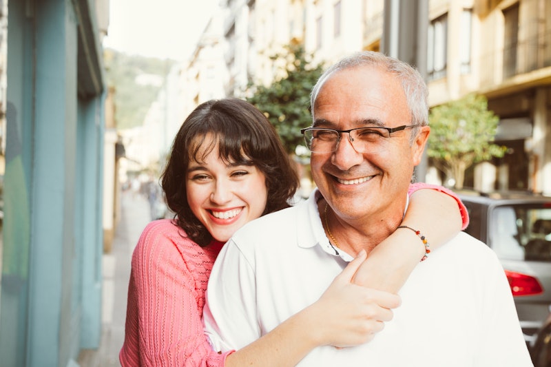 A woman smiles while wrapping her arms around her dad on a sunny day.