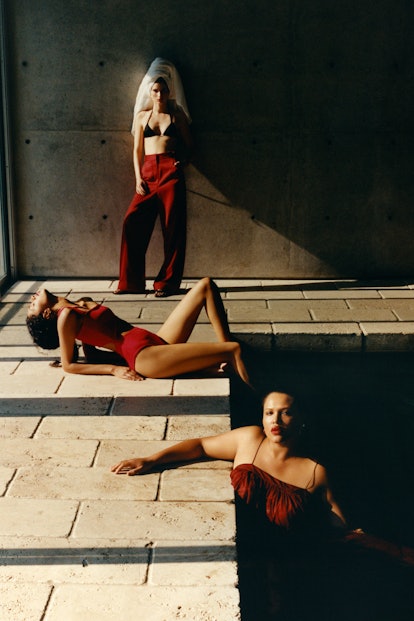 Three women in red summer dresses stand next to a dark pool