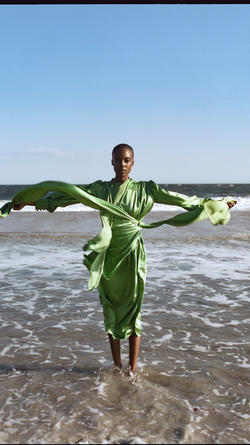A model posing in a satin light-green Gucci dress on a beach