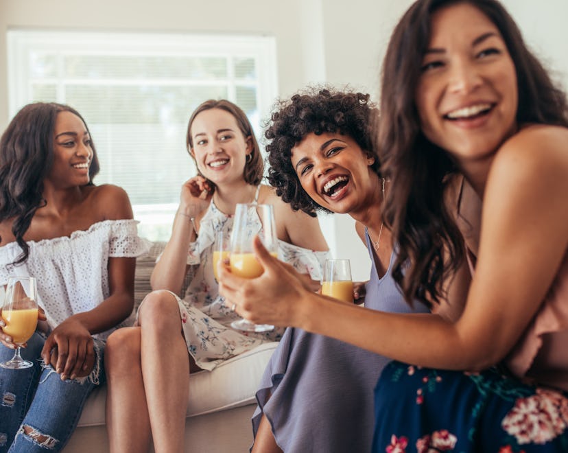 Four women at a rainbow baby shower, sitting and smiling while holding their drinks.