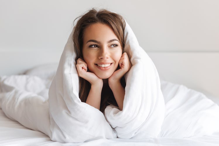 A young woman wrapped up in white sheets while lying on the bed.
