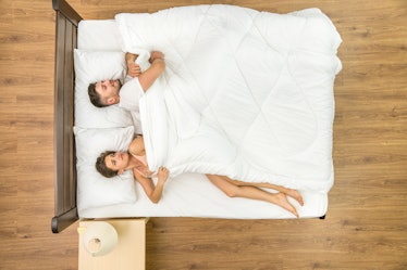 A woman in bed looking at her partner taking cover for himself