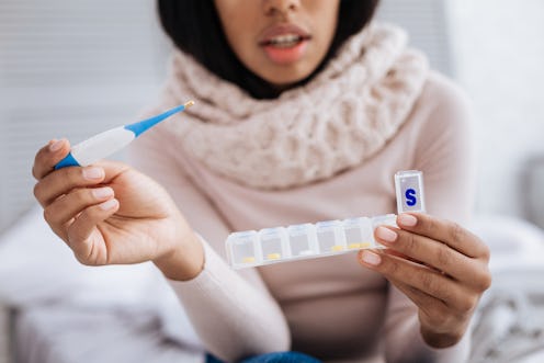 A woman with a thermometer opens a weekly pill container. These 7 foods can make your flu symptoms f...