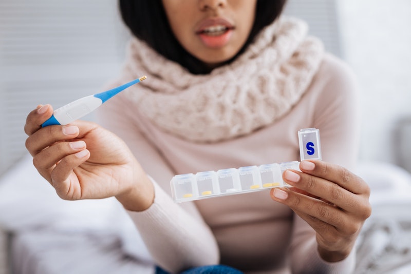 A woman with a thermometer opens a weekly pill container. These 7 foods can make your flu symptoms f...