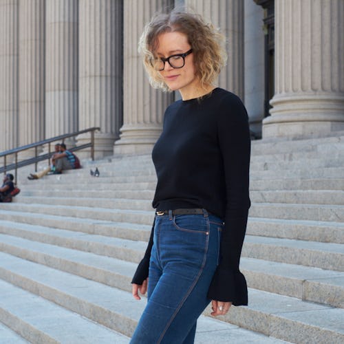 A woman with a blonde curly hair and glasses, wearing a black sweater and blue jeans walking down th...