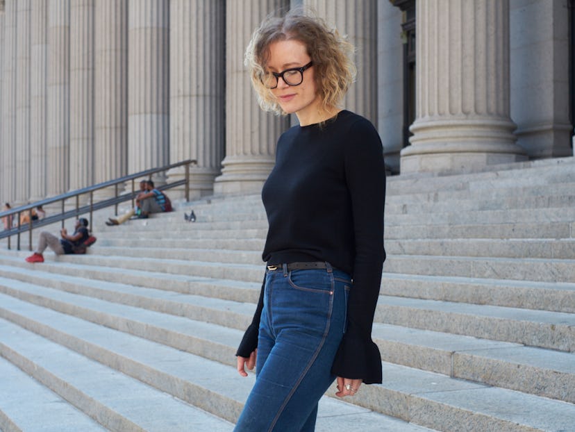 A woman with a blonde curly hair and glasses, wearing a black sweater and blue jeans walking down th...