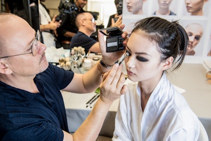 A model sitting backstage getting Dior Haute Couture Fall/Winter 2019's Makeup Look applied by a mak...