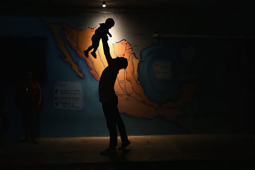 A parent holding a child high up in a dark space with a single light showing their silhouette 