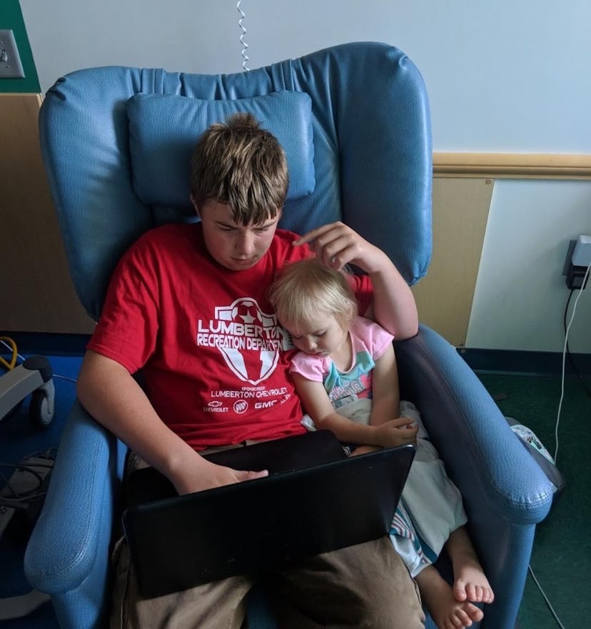 Marie Amsdill's oldest son helps his sister with a video on the laptop in the hospital room of her y...