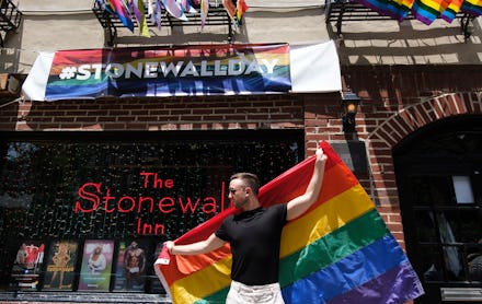 A man holding the LGBTQ+ flag on a street