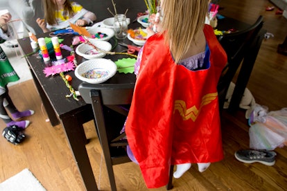 A girl wearing a Wonder Woman cape making a mask on a birthday party