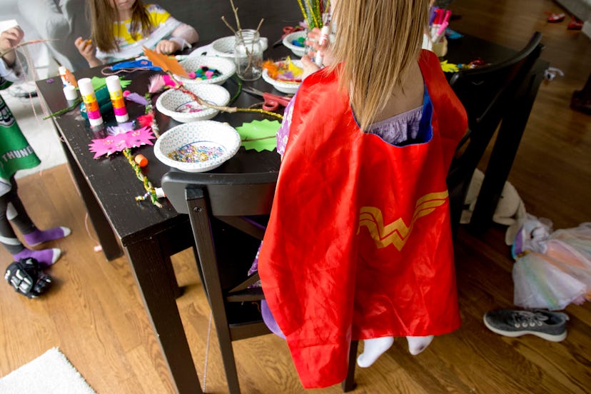 A girl wearing a Wonder Woman cape making a mask on a birthday party