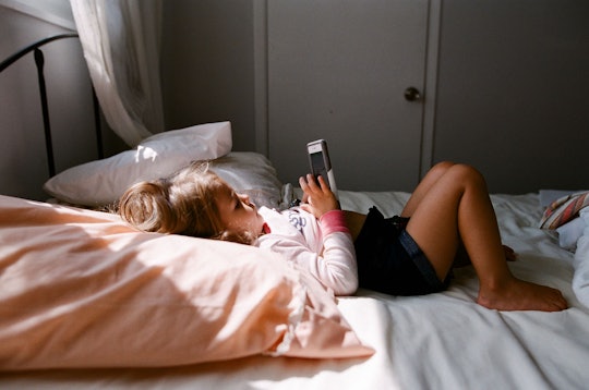 A girl lying in bed while using her phone, sunlight is beaming down on her through the window