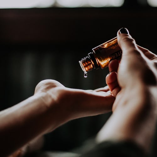 a pair of hands in front of a black background applying a skin serum