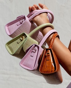 A hand with four leather handbags on it, pink, green and brown