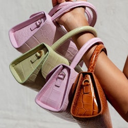 A hand with four leather handbags on it, pink, green and brown