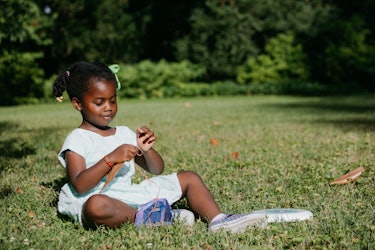 A 4-year-old Sloane wearing a white dress while sitting on a grass and playing