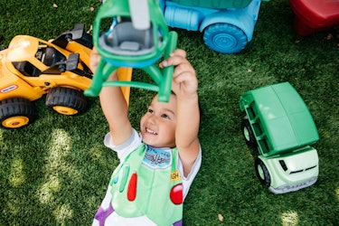 Ferris lying on the grass surrounded by his toys while holding his plastic helicopter in the air