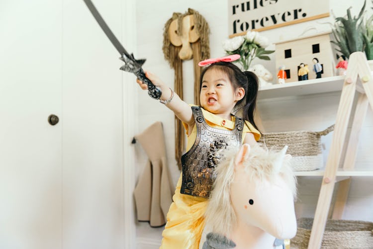 A 3-year-old Joey dressed as a warrior sitting on her white plush unicorn while holding her sword in...