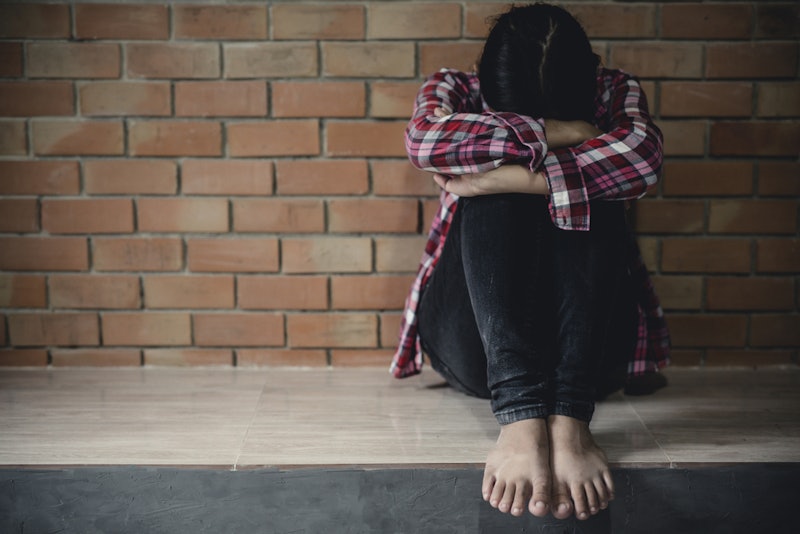 A barefoot woman holding her knees while sitting in front of a brick wall because of her anxiety