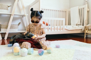 Joey, with space buns and sunglasses, wearing a beige floral-patterned dress while playing with her ...