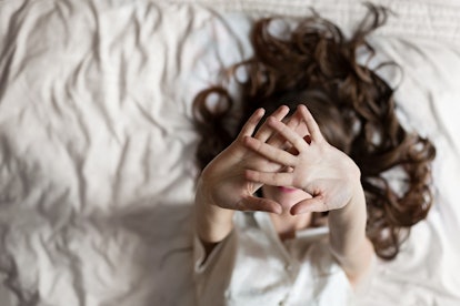 A woman with anxiety holding her hands stretched out in front of her face while lying in bed not sle...