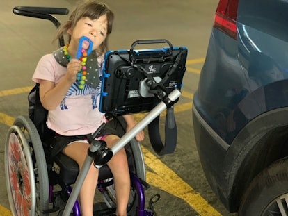 A girl in a wheelchair playing with a brightly colored toy and looking at a screen mounted in front ...
