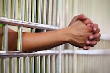 The hands of a brown trans person pulled through jail bars