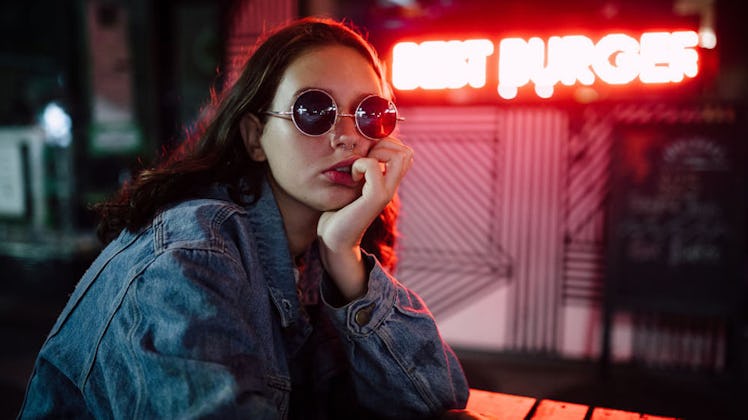 Young woman wearing sunglasses in front of neon sign that says Best Burger.