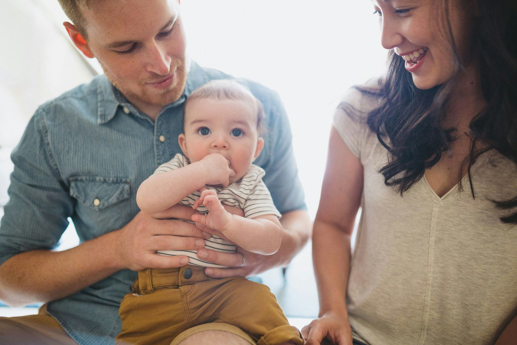 A dad holding a baby and the mom sitting next to them and smiling eve though she is struggling