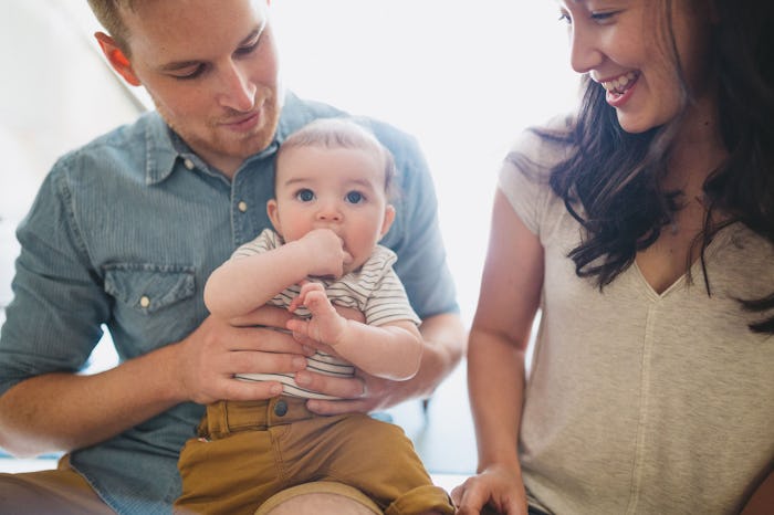 A dad holding a baby and the mom sitting next to them and smiling eve though she is struggling