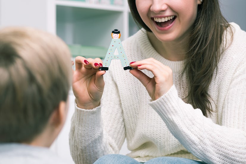 A mom smiling and showing an 'A' toy to her child with autism