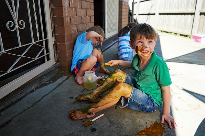 Three boys sitting on a garden floor with their legs covered in paint.