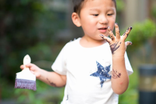 A boy holding a paint brush looking at his hand covered in black paint