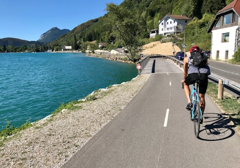 A person on a bicycle ride nest to a body of water on a bike lane next to the road