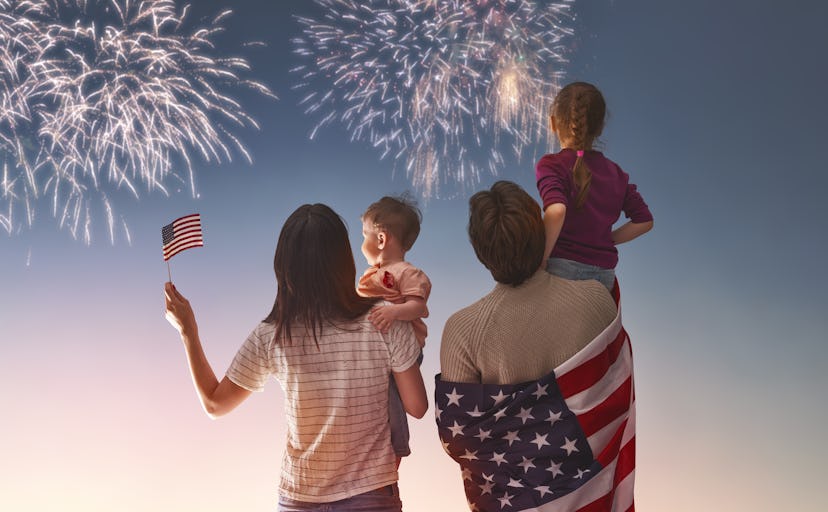 A family of four holding flags of the USA while watching fireworks