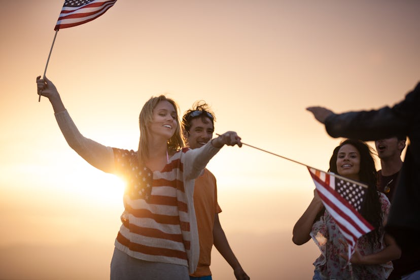 A blonde woman wearing t-shirt with the flag of the USA and holding two flags while celebrating the ...