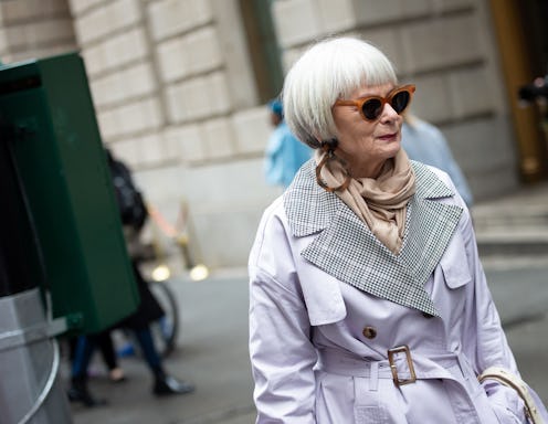A woman over 50 in the fall, wearing a long jacket, scarf and sunglasses