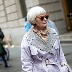 A woman over 50 in the fall, wearing a long jacket, scarf and sunglasses