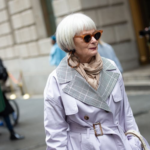 A woman over 50 in the fall, wearing a long jacket, scarf and sunglasses