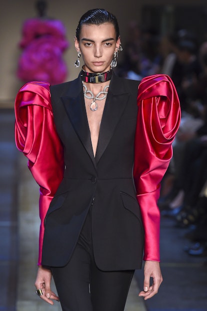 A model on a runway in a black blazer with red satin puff sleeves and black pants during Fall