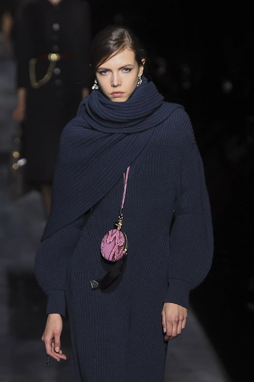 A model on a runway in a navy sweater-dress and a pink micro-bag