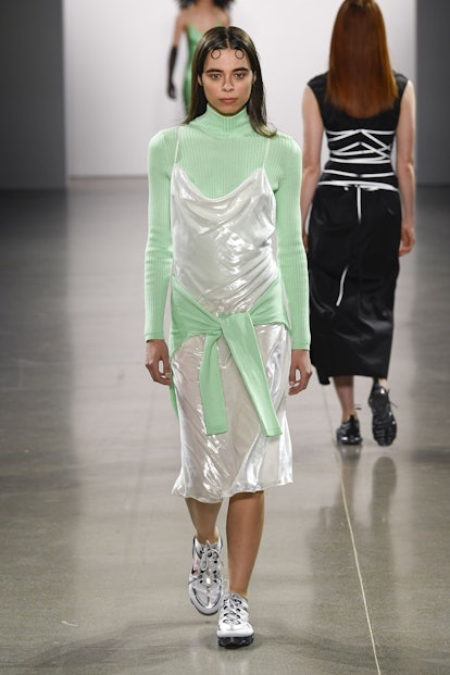 A model on a runway in a lime turtleneck and a silver slip dress