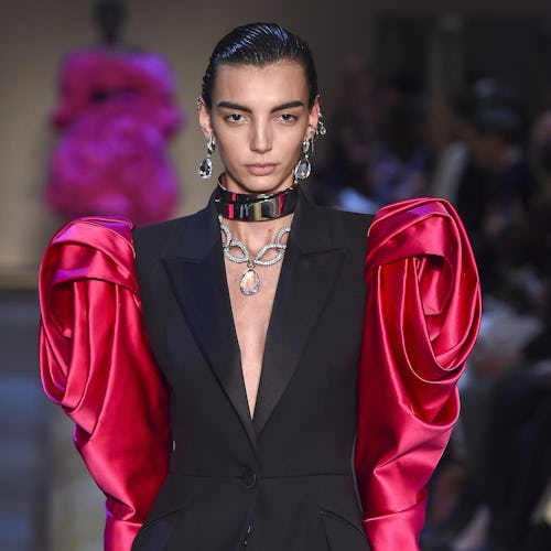 A model on a runway in a black blazer with red satin puff sleeves during Fall