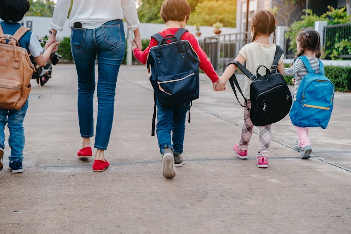 A view from behind of a mom taking her four kids to school drop off as they all hold hands