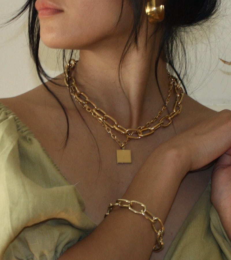 A woman in a beige top with a thick chain necklace and thing necklace, and a thick chain bracelet
