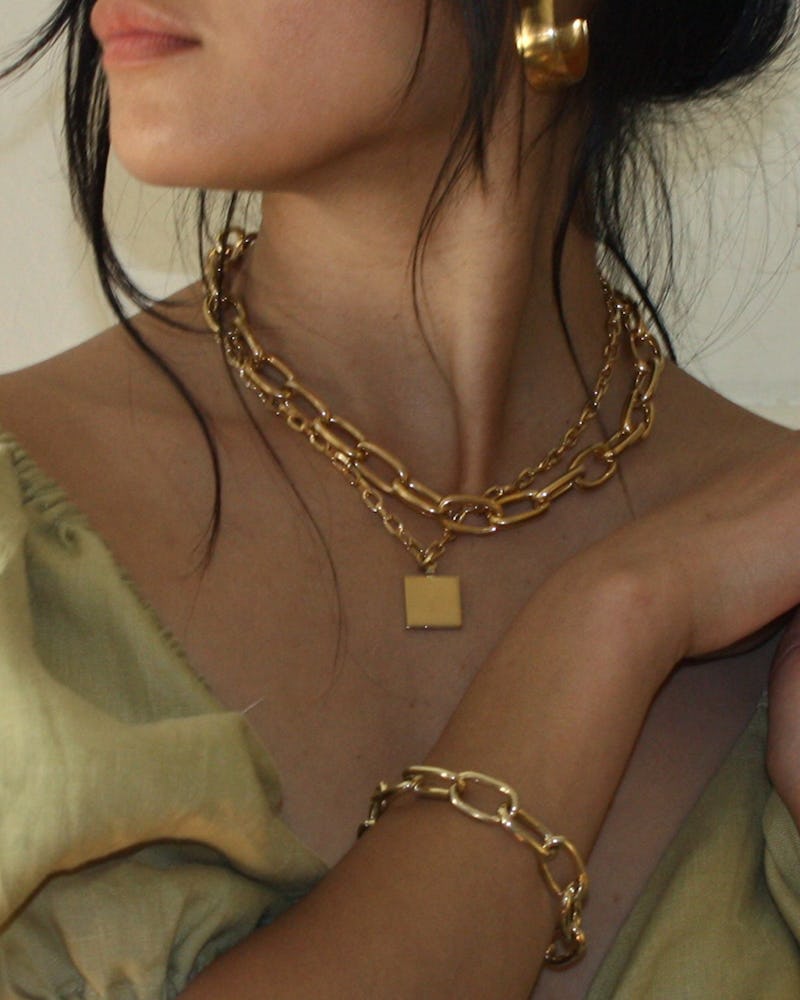 A woman in a beige top with a thick chain necklace and thing necklace, and a thick chain bracelet