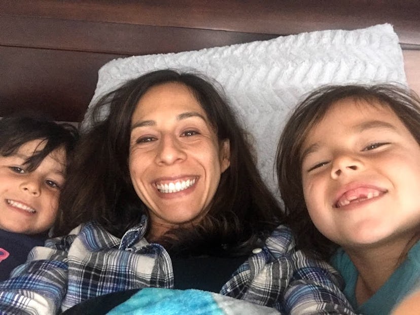 A mother and two children lying in bed smiling while taking a selfie