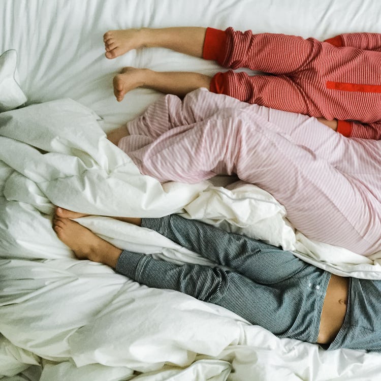 A woman lying in bed in pink pajamas with two children to either side of her in red and green pajama...